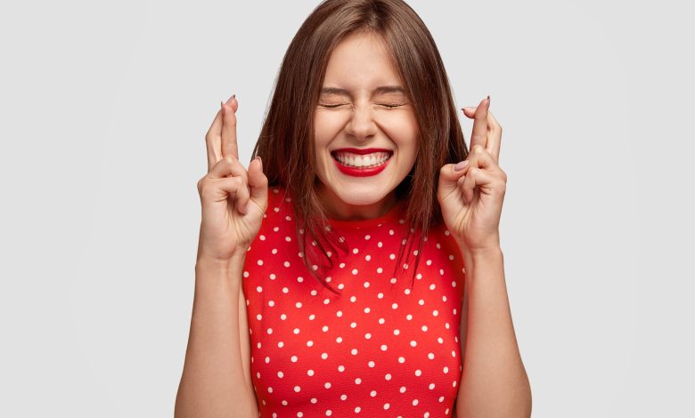 pleased attractive european woman makes wish to win raises hands with crossed fingers waits for lottery results closes eyes